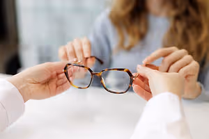 A person is holding a pair of glasses and examining them closely.