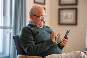 Elderly man sitting on a chair using a cell phone