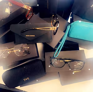 A pile of Dolce and Gabbana brand accessories including glasses, a clutch bag, and a wallet on a table