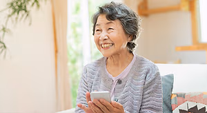 Older woman sitting on a couch and smiling while looking at her phone