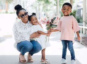 A mother and her two kids, a boy and a girl, are posing for a photo, holding flowers and smiling