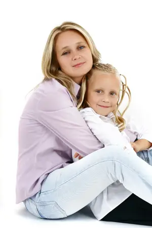 A woman and a little girl are sitting close to each other and smiling for a photo.