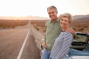 A couple standing next to a vintage car in a desert landscape with mountains in the distance