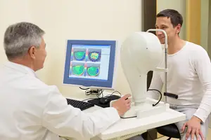 A doctor wearing a white coat examines a patient wearing a white shirt in an eye clinic.