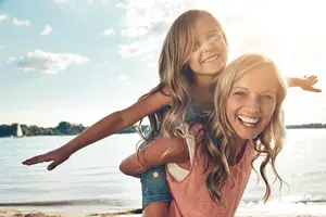 A woman carrying a child on her shoulder with a big smile on her face