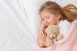 A young girl sleeping on a bed with a teddy bear