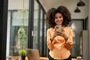 A woman is standing in an office and holding a cell phone in her hand