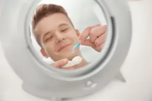A man puts a contact lens in his eye while looking in a mirror