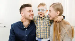 A smiling family with a young boy wearing glasses posing for a photo in a room with white walls