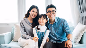 A family of three sitting on a couch in a living room with pillows and smiling at the camera