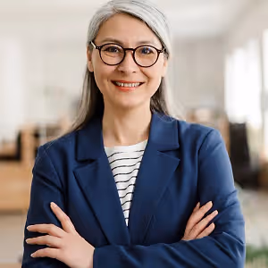 Smiling woman with glasses and a blue blazer standing in an office room