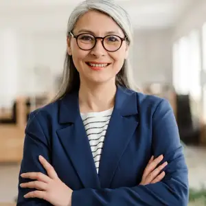 Smiling woman with glasses and a blue blazer standing in an office room