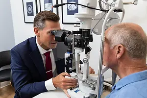 A doctor using a phoropter to examine an older man's eyes.