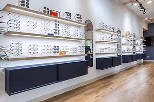 The interior of a glasses shop with a wall of shelves of eyeglasses on display with a sign that says '10% OFF' and a large plant in the corner.