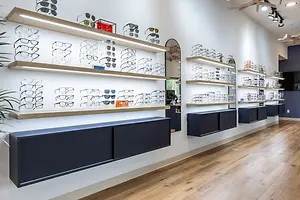 The interior of a glasses shop with a wall of shelves of eyeglasses on display with a sign that says '10% OFF' and a large plant in the corner.