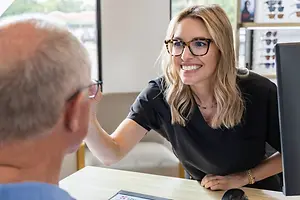 Woman optician wearing glasses and a black top helping a male customer in a glasses store
