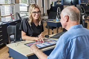 Woman in glasses explaining something on a tablet to a man in a blue shirt in a retail setting