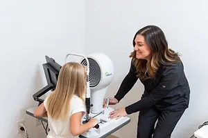 A woman doctor is examining a child's eyes with a machine in an indoor area.
