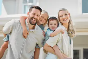 A family of four is smiling and posing for a photo in front of their house
