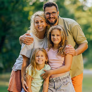 A family of four is smiling in a park with trees in the background