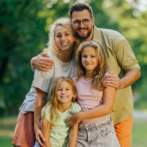 A family of four is smiling in a park with trees in the background