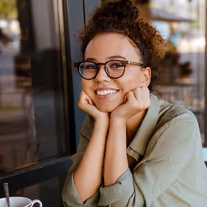 A woman sitting in a cafe with glasses on and smiling