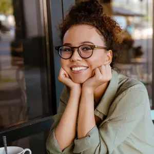 A woman sitting in a cafe with glasses on and smiling