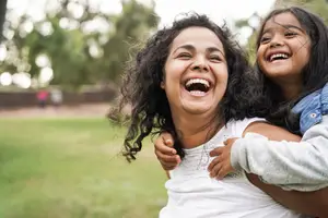 Two girls, one holding the other and both are laughing