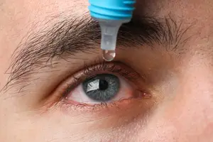 A close-up of a man's eye with a drop of eyedropper liquid being applied