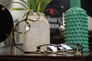 Three pairs of glasses on a wooden table with a vase and plant in the background