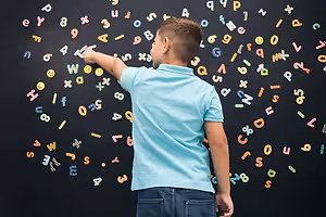 A boy during Vision Therapy session, standing and pointing at a blackboard with alphabets and numbers arranged in a spiral pattern