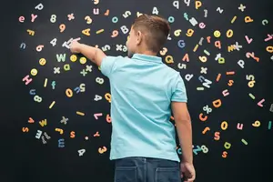 A boy during Vision Therapy session, standing and pointing at a blackboard with alphabets and numbers arranged in a spiral pattern