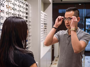 A man is adjusting glasses in a store with a woman standing next to him.