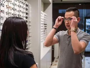 A man is adjusting glasses in a store with a woman standing next to him.