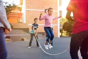 Three children jump rope together on a driveway with a building in the background.