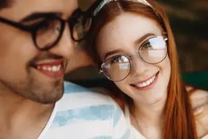 A young man and woman sitting on a bench looking at each other smiling with their teeth showing