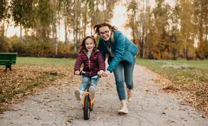 A woman helps a girl ride a bicycle in a park during autumn