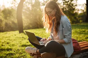 A woman sitting on a bench with a laptop in the park