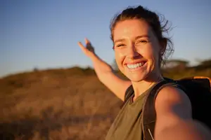 A smiling woman in a field waving her hand and looking at the camera
