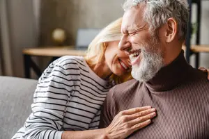 An older man and woman sitting on a couch smiling and hugging each other
