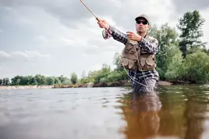 A man fishing in a river with trees and a cloudy sky in the background