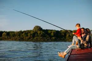 A family is fishing on a dock with a young child holding a fishing rod in a red shirt