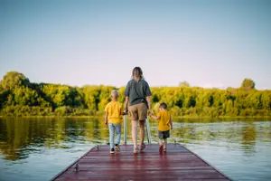 A woman and two kids standing on a wooden dock by the lake during the daytime