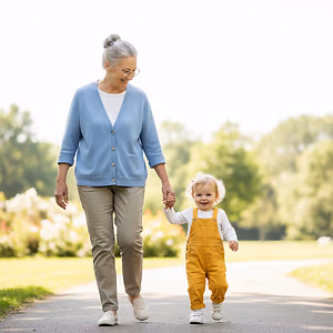 An older woman and a toddler are walking down a sidewalk in a park together.