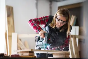 A woman using a circular saw on a wooden plank in a workshop