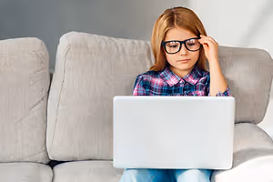 A girl sitting on a couch while using a laptop