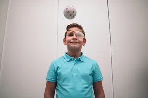 A young boy with an eye patch is looking up at a ball with letters on it.