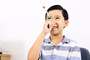 A boy is playing with a toothbrush and smiling at the camera while sitting on a chair