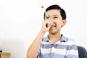 A boy is playing with a toothbrush and smiling at the camera while sitting on a chair