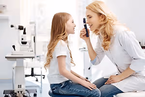 A woman wearing a white lab coat is examining the eyes of a young girl in a clinic.